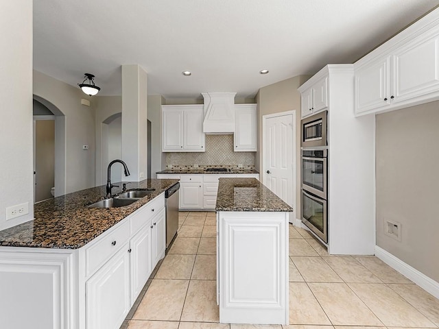 kitchen featuring a center island, custom range hood, appliances with stainless steel finishes, light tile patterned flooring, and a sink