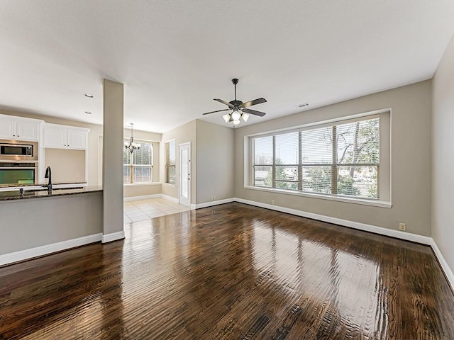 unfurnished living room with visible vents, a sink, wood finished floors, baseboards, and ceiling fan with notable chandelier