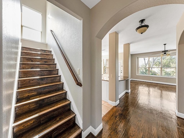 stairs with a ceiling fan, arched walkways, baseboards, and wood finished floors