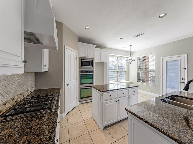 kitchen with stainless steel appliances, visible vents, white cabinetry, a sink, and wall chimney range hood