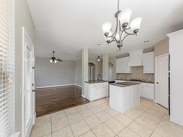 kitchen with light tile patterned floors, arched walkways, decorative backsplash, custom range hood, and a sink