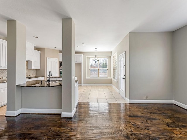 kitchen with baseboards, decorative backsplash, oven, white cabinetry, and a sink