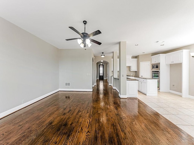 unfurnished living room featuring baseboards, visible vents, arched walkways, ceiling fan, and light wood-style floors