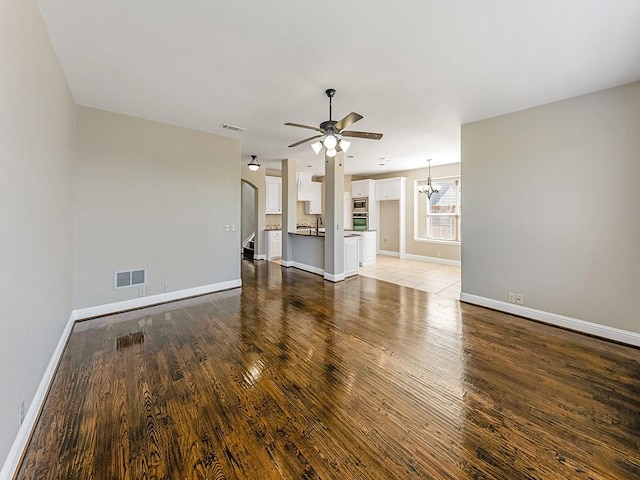 unfurnished living room with baseboards, ceiling fan with notable chandelier, and light wood-style floors