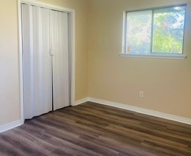 unfurnished bedroom with a closet, dark wood-style flooring, and baseboards