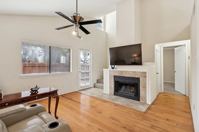 living area with a ceiling fan, a tile fireplace, wood-type flooring, and a towering ceiling