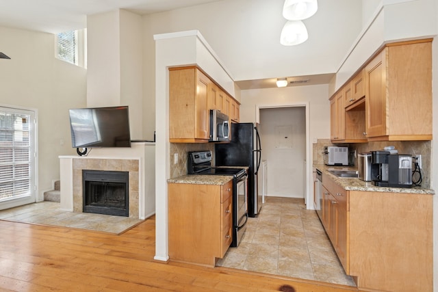 kitchen featuring electric range, a fireplace, light wood-type flooring, decorative backsplash, and stainless steel microwave