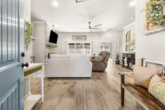 living area with light wood finished floors, a fireplace, arched walkways, and crown molding