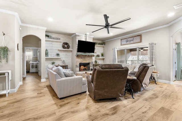 living room featuring arched walkways, ornamental molding, light wood finished floors, and a fireplace