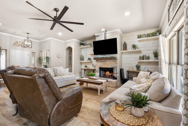 living room with arched walkways, a fireplace, recessed lighting, ornamental molding, and light wood-style floors