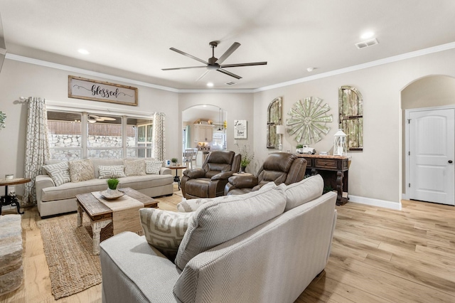 living area featuring light wood-style floors, arched walkways, visible vents, and crown molding