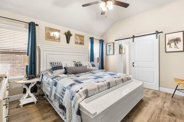 bedroom featuring vaulted ceiling, a barn door, light wood finished floors, and baseboards