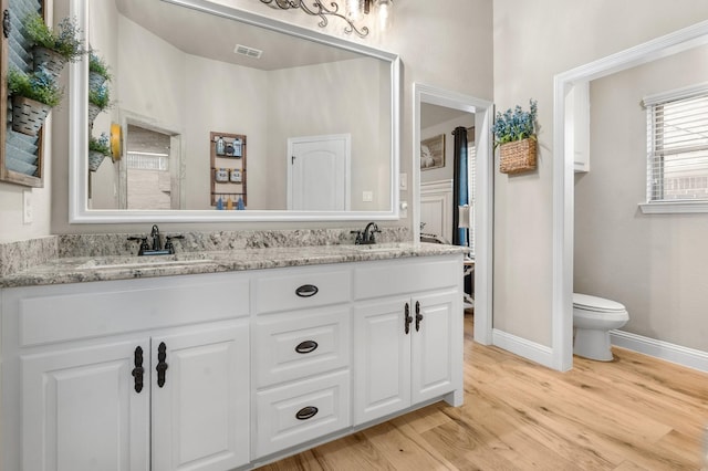 full bathroom with double vanity, baseboards, visible vents, toilet, and wood finished floors