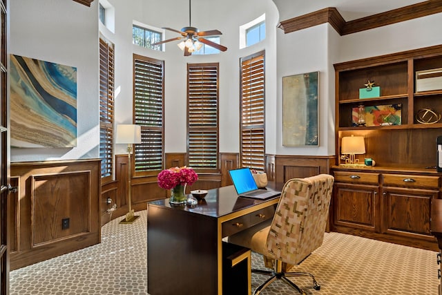 home office featuring carpet, ornamental molding, a ceiling fan, and wainscoting