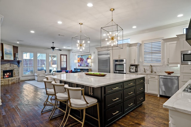 kitchen featuring dark wood finished floors, built in appliances, a stone fireplace, white cabinetry, and a sink