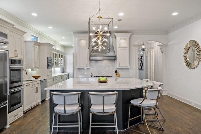 kitchen featuring arched walkways, crown molding, stainless steel appliances, an inviting chandelier, and a kitchen bar