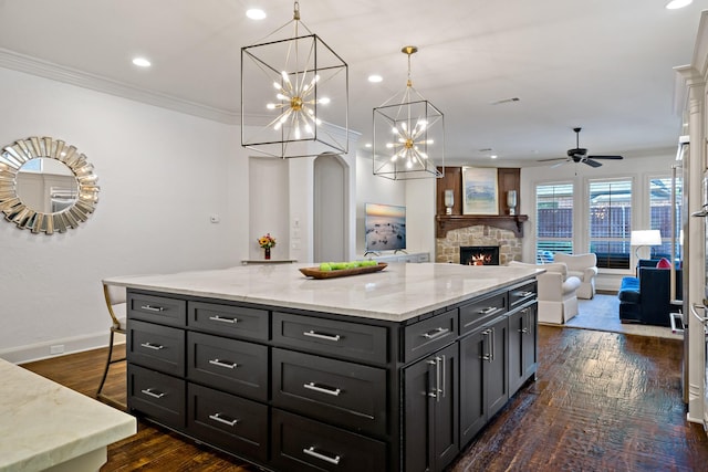 kitchen with a kitchen island, ornamental molding, dark wood-style flooring, dark cabinetry, and a fireplace