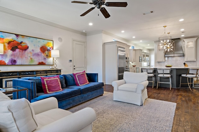 living area with dark wood-style floors, recessed lighting, visible vents, ornamental molding, and ceiling fan with notable chandelier