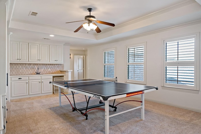 recreation room featuring light colored carpet, beverage cooler, visible vents, ornamental molding, and a tray ceiling