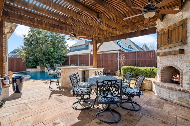 view of patio / terrace featuring a ceiling fan, a fenced backyard, an outdoor stone fireplace, a pergola, and outdoor dining space