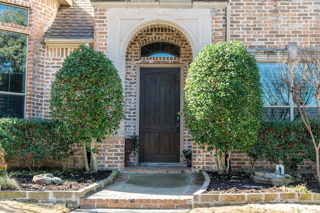 view of exterior entry with brick siding and roof with shingles