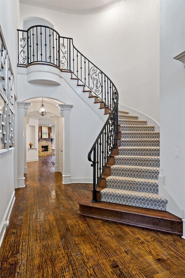 entrance foyer with a high ceiling, a fireplace, wood finished floors, baseboards, and ornate columns