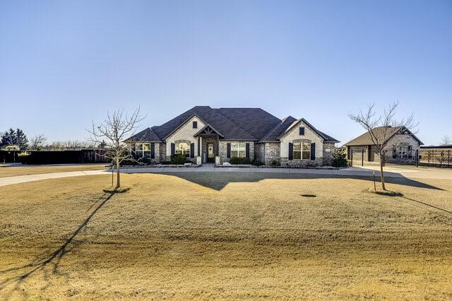 french country style house featuring stone siding and a front lawn