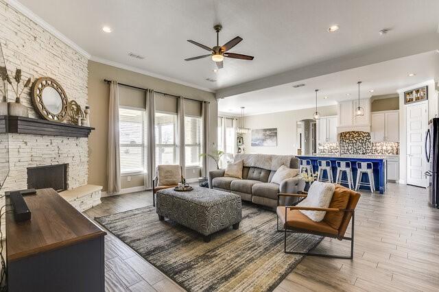 living room with visible vents, a ceiling fan, ornamental molding, wood finished floors, and a fireplace