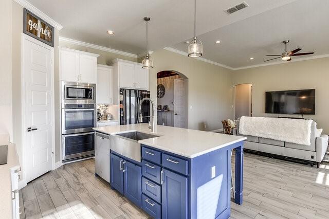 kitchen featuring arched walkways, visible vents, white cabinetry, blue cabinetry, and appliances with stainless steel finishes