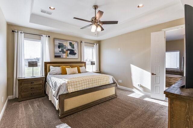 bedroom featuring a tray ceiling, visible vents, and baseboards