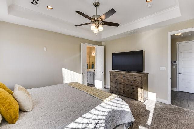 bedroom with ensuite bath, visible vents, baseboards, and a raised ceiling