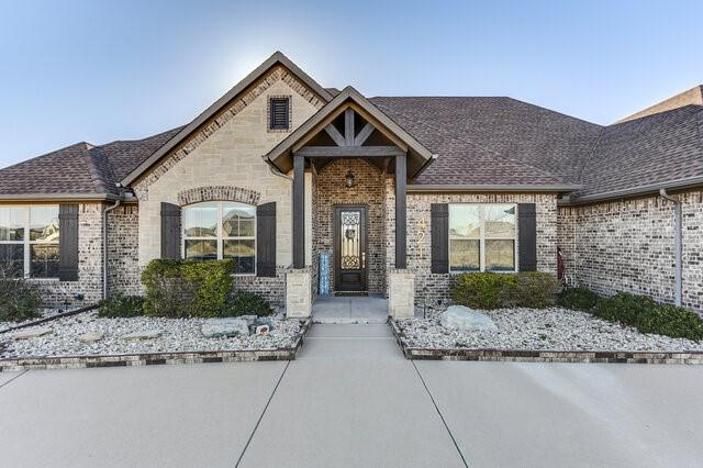 french country home featuring a shingled roof and brick siding