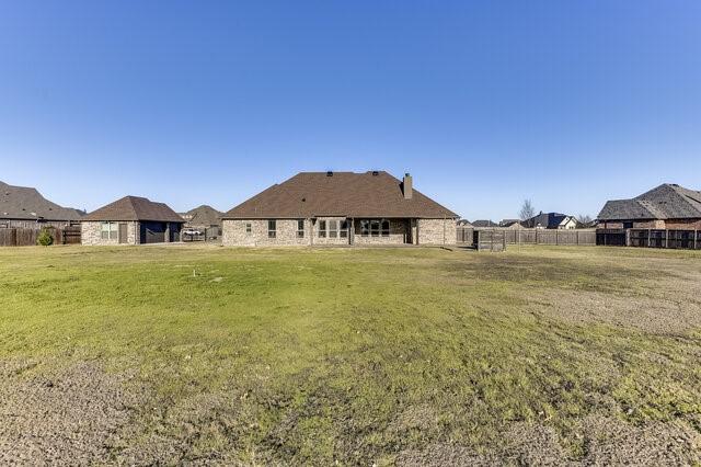 rear view of property featuring a lawn and fence