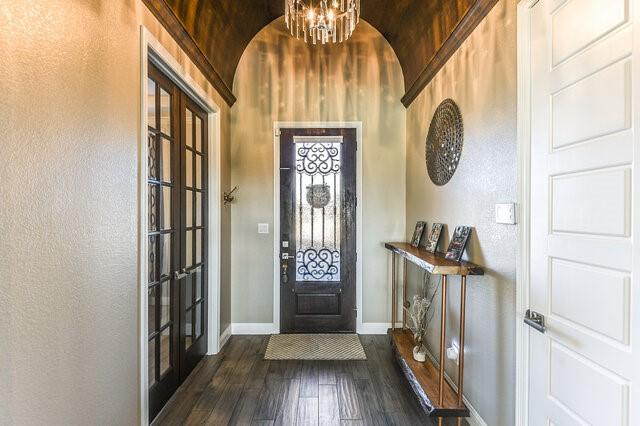 foyer entrance featuring dark wood-style floors, a chandelier, a textured wall, and baseboards