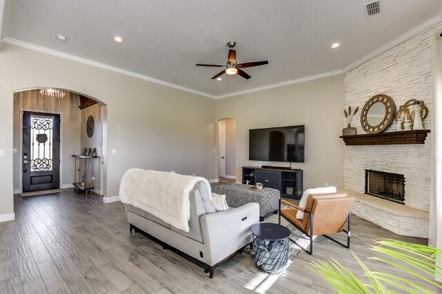 living area with baseboards, arched walkways, wood finished floors, crown molding, and a stone fireplace