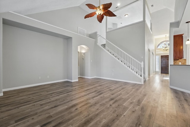 unfurnished living room featuring arched walkways, ceiling fan with notable chandelier, dark wood-style flooring, visible vents, and stairs