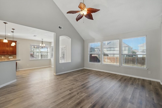 unfurnished living room with baseboards, visible vents, wood finished floors, high vaulted ceiling, and ceiling fan with notable chandelier