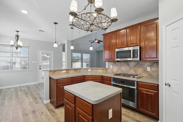 kitchen with decorative light fixtures, stainless steel appliances, light countertops, light wood-type flooring, and backsplash