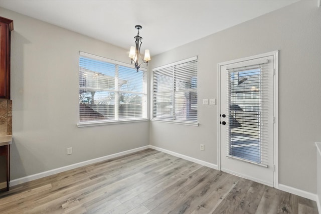 unfurnished dining area featuring light wood-type flooring, a notable chandelier, and baseboards