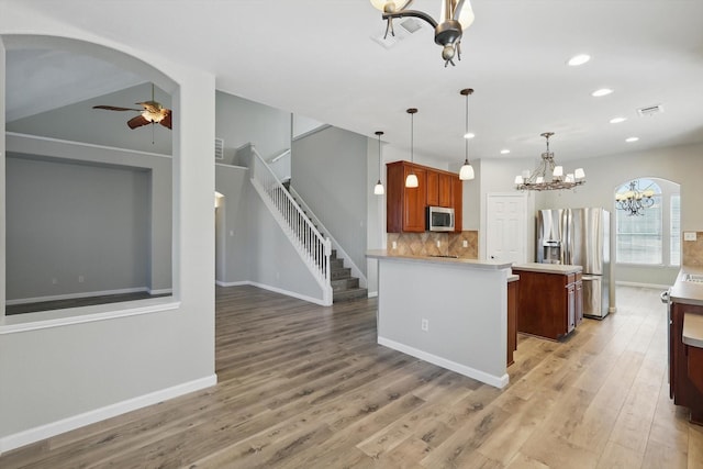 kitchen with light wood-style flooring, ceiling fan with notable chandelier, light countertops, appliances with stainless steel finishes, and tasteful backsplash