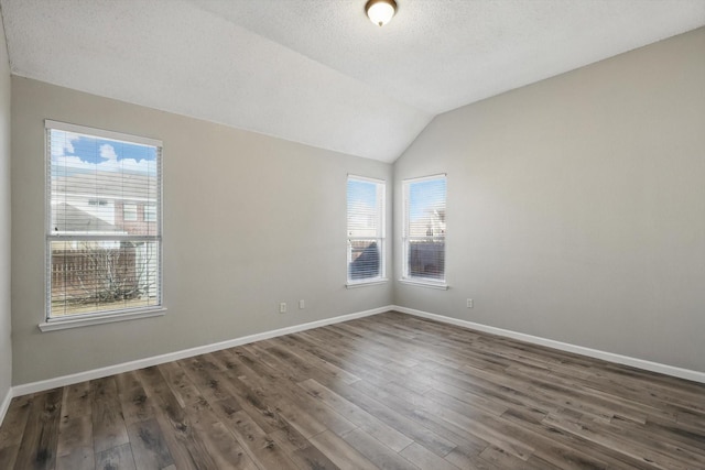 unfurnished room with a textured ceiling, baseboards, vaulted ceiling, and wood finished floors