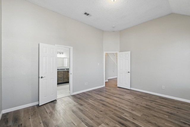 unfurnished bedroom with ensuite bath, wood finished floors, visible vents, and baseboards