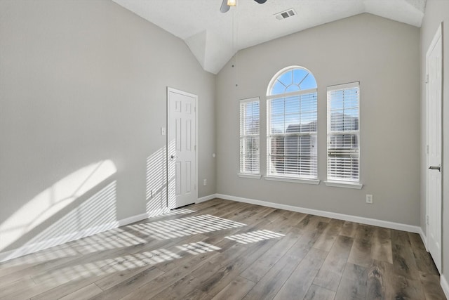 empty room with vaulted ceiling, wood finished floors, visible vents, and a ceiling fan