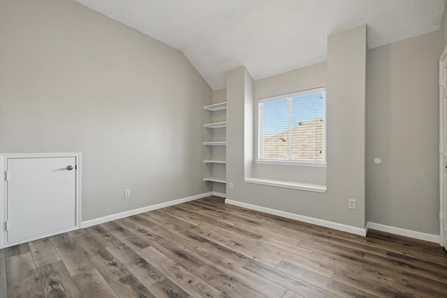 empty room featuring baseboards, vaulted ceiling, and wood finished floors