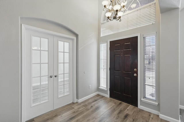 foyer entrance with a notable chandelier, baseboards, wood finished floors, and french doors