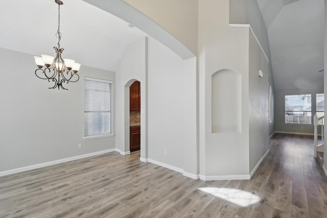 interior space featuring arched walkways, a notable chandelier, high vaulted ceiling, light wood-type flooring, and baseboards