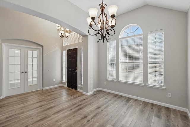 entrance foyer with a chandelier, lofted ceiling, wood finished floors, baseboards, and french doors