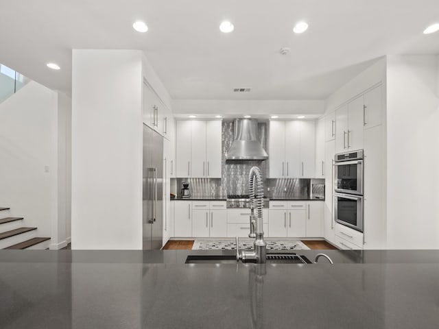 kitchen featuring tasteful backsplash, dark countertops, wall chimney exhaust hood, stainless steel appliances, and a sink