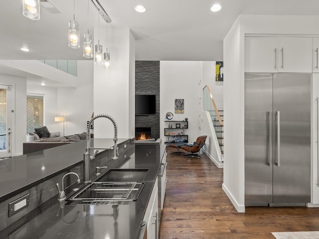 kitchen with built in fridge, dark countertops, open floor plan, a large fireplace, and a sink