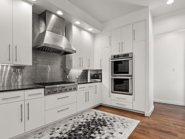 kitchen featuring tasteful backsplash, dark countertops, appliances with stainless steel finishes, wall chimney range hood, and baseboards